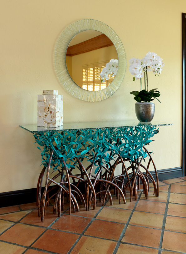 An Oceanside foyer with a copper mangrove console table and wavy framed mirror